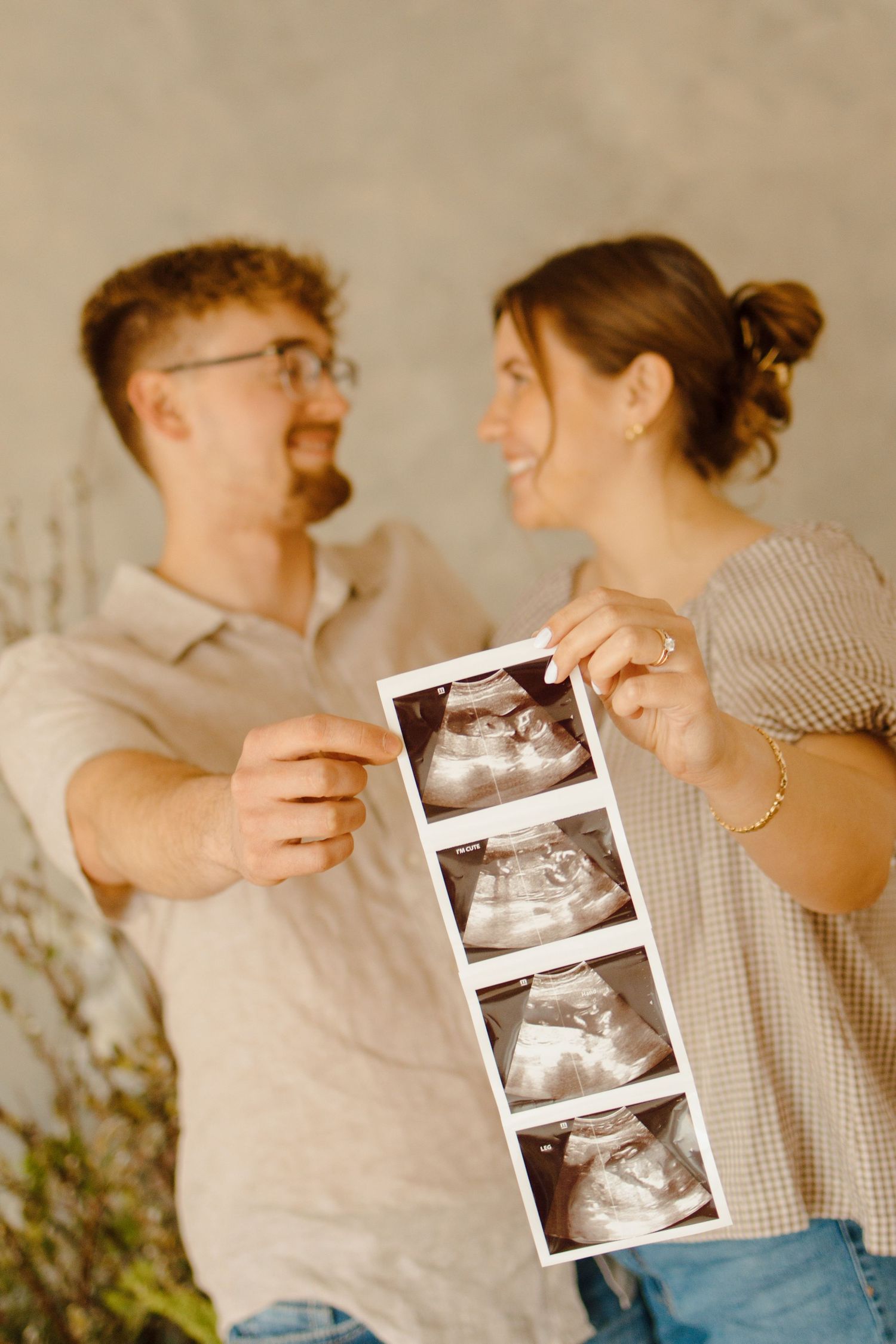 Happy couple smiling and holding ultrasound photos, announcing pregnancy with sonogram strip.