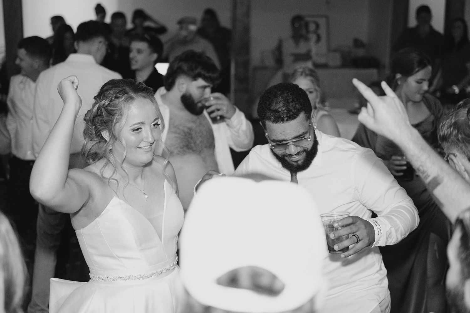 Bride and groom laugh and dance joyfully with guests at lively black and white wedding reception.