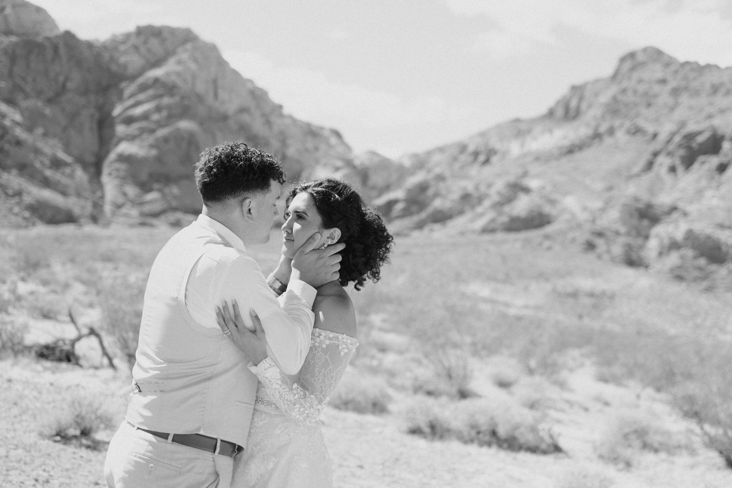 A tender black and white photo of a couple sharing an intimate moment against a desert mountain landscape background.