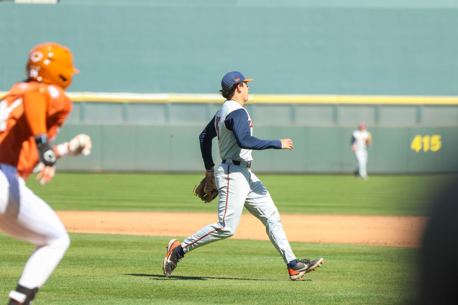 Baseball player in dark uniform and cap strides forward while pitching on green baseball field during daytime game.
