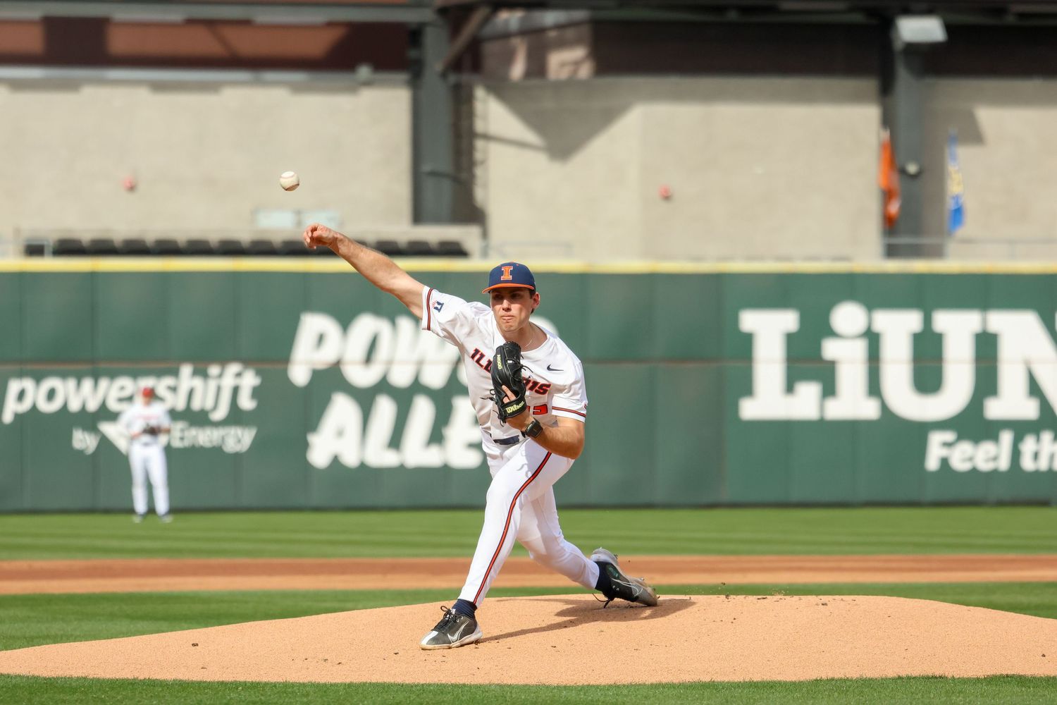 Baseball pitcher in white uniform winds up to throw from the mound during a game at an outdoor stadium.