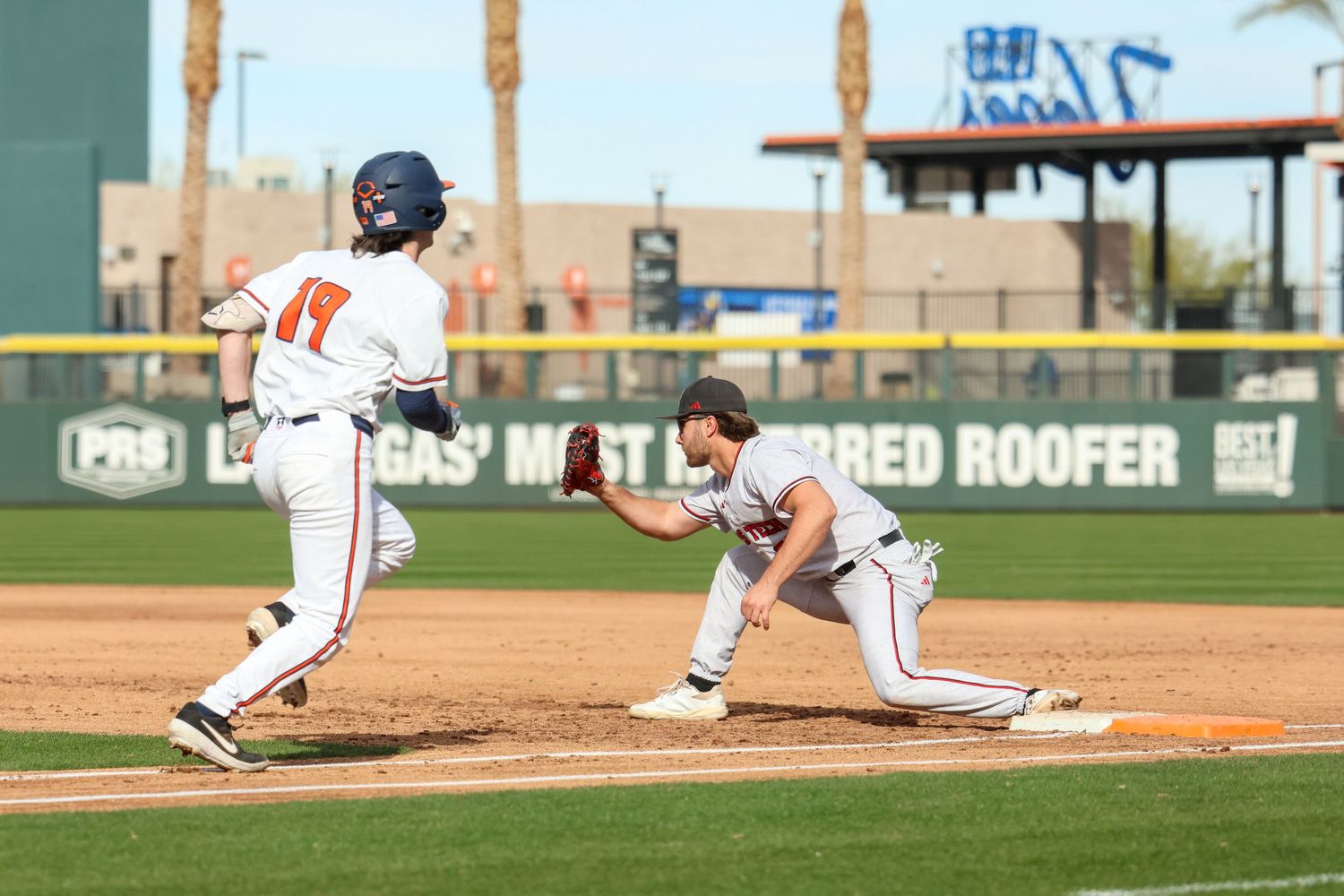 Baseball game play showing runner leading off first base with fielder in defensive position.