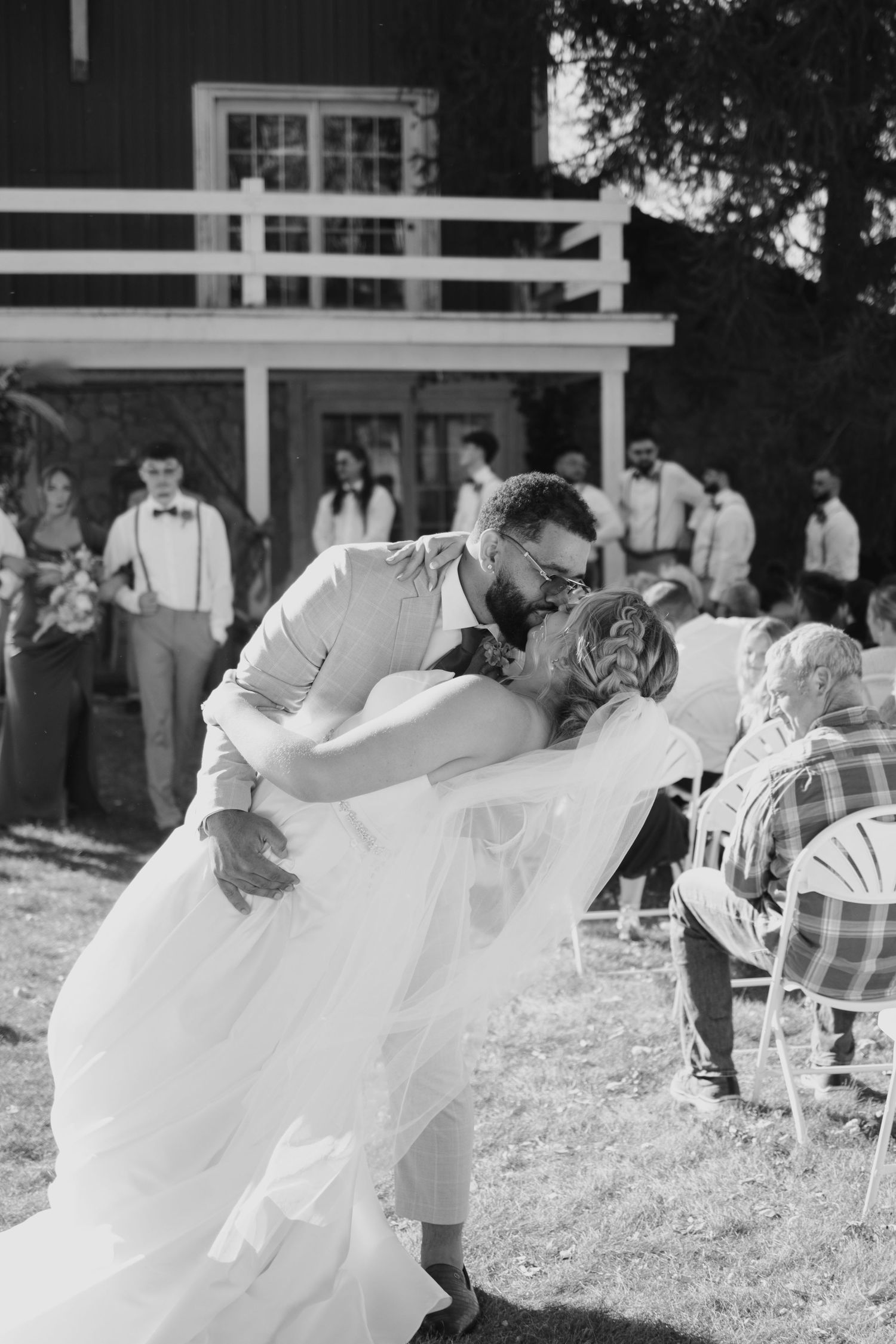 Groom dips bride for a kiss during outdoor wedding ceremony in black and white photo.
