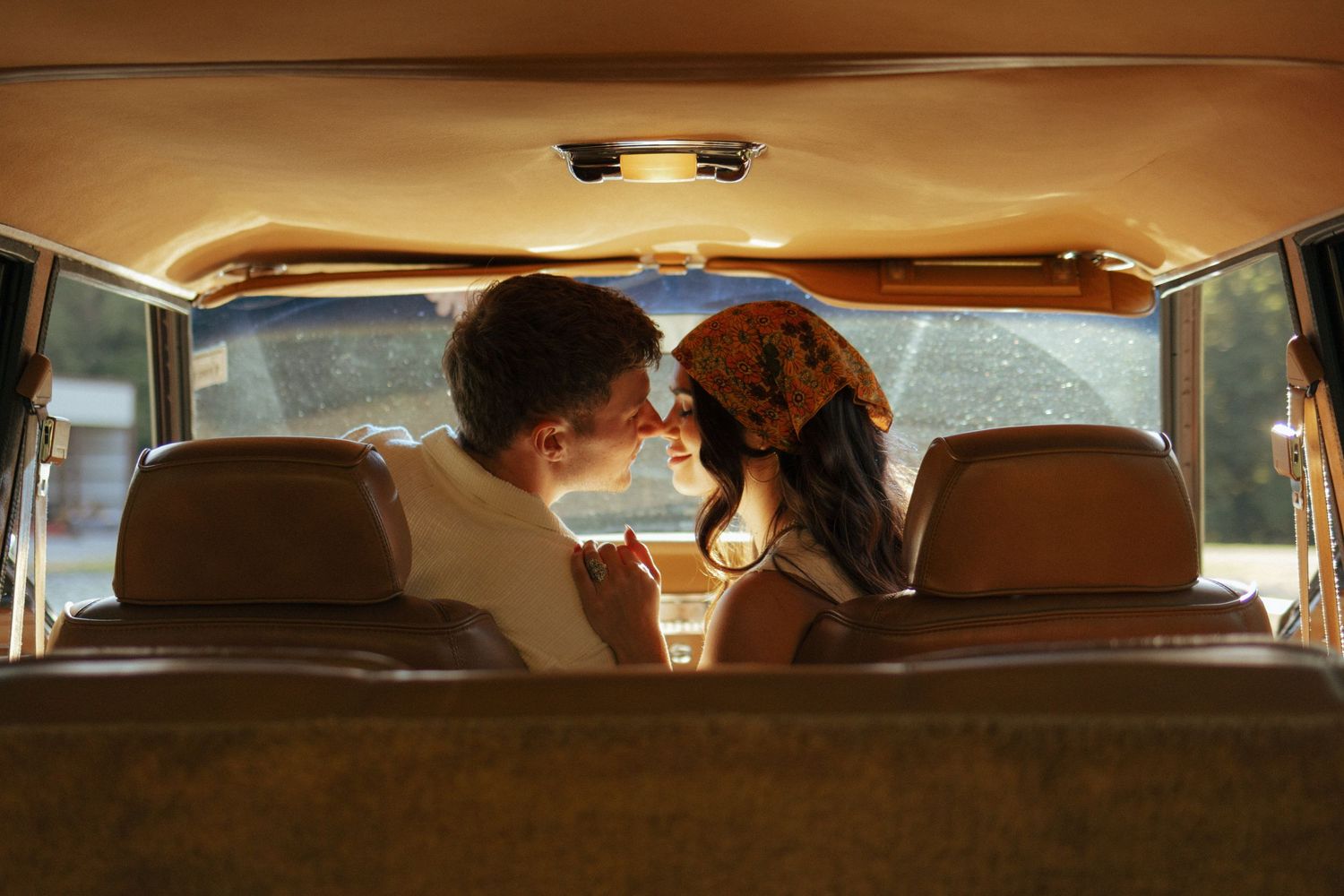 Romantic couple sharing an intimate moment kissing in the back seat of a vintage car.