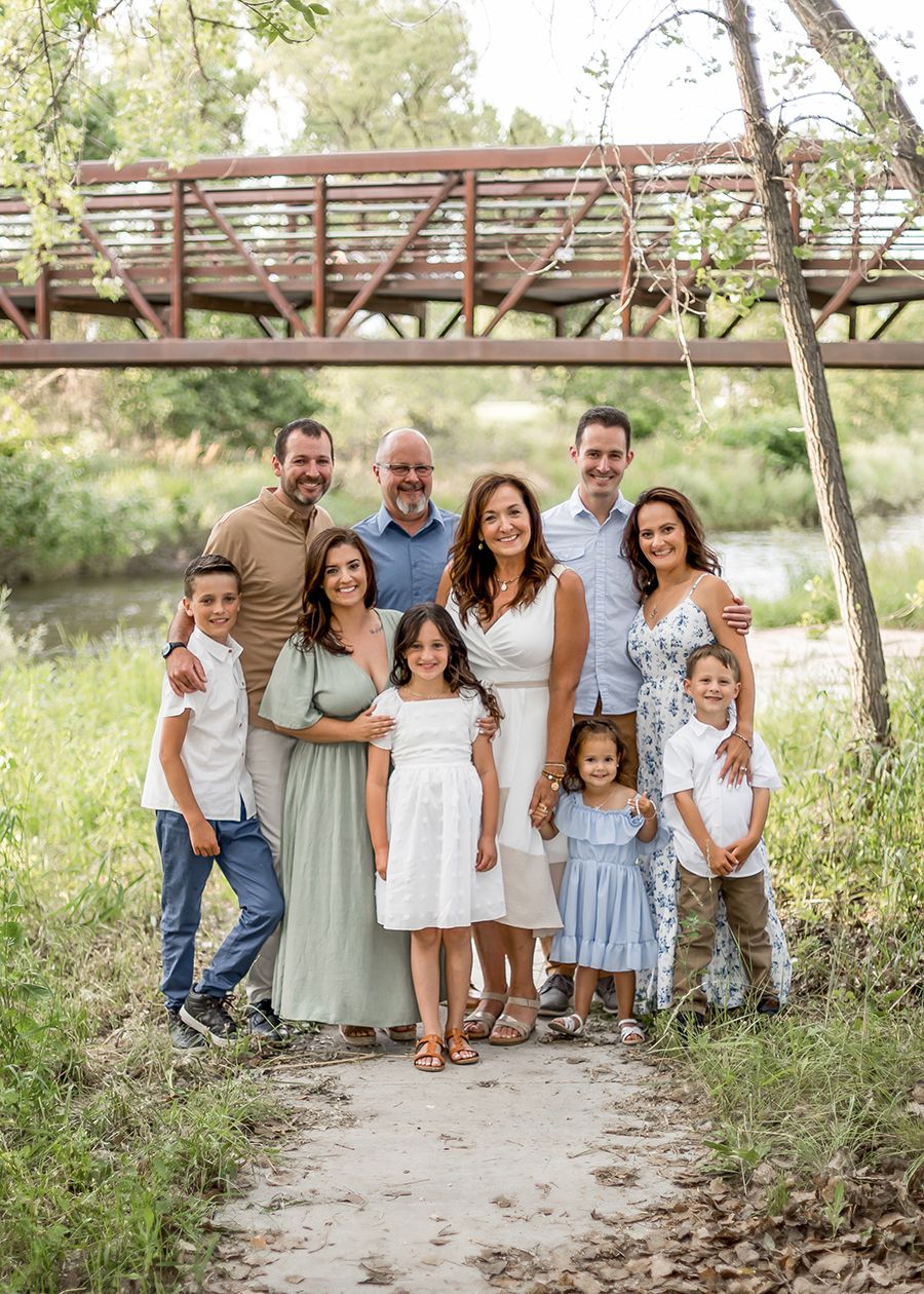Large family group portrait outdoors on a nature path with a bridge backdrop on a sunny day.