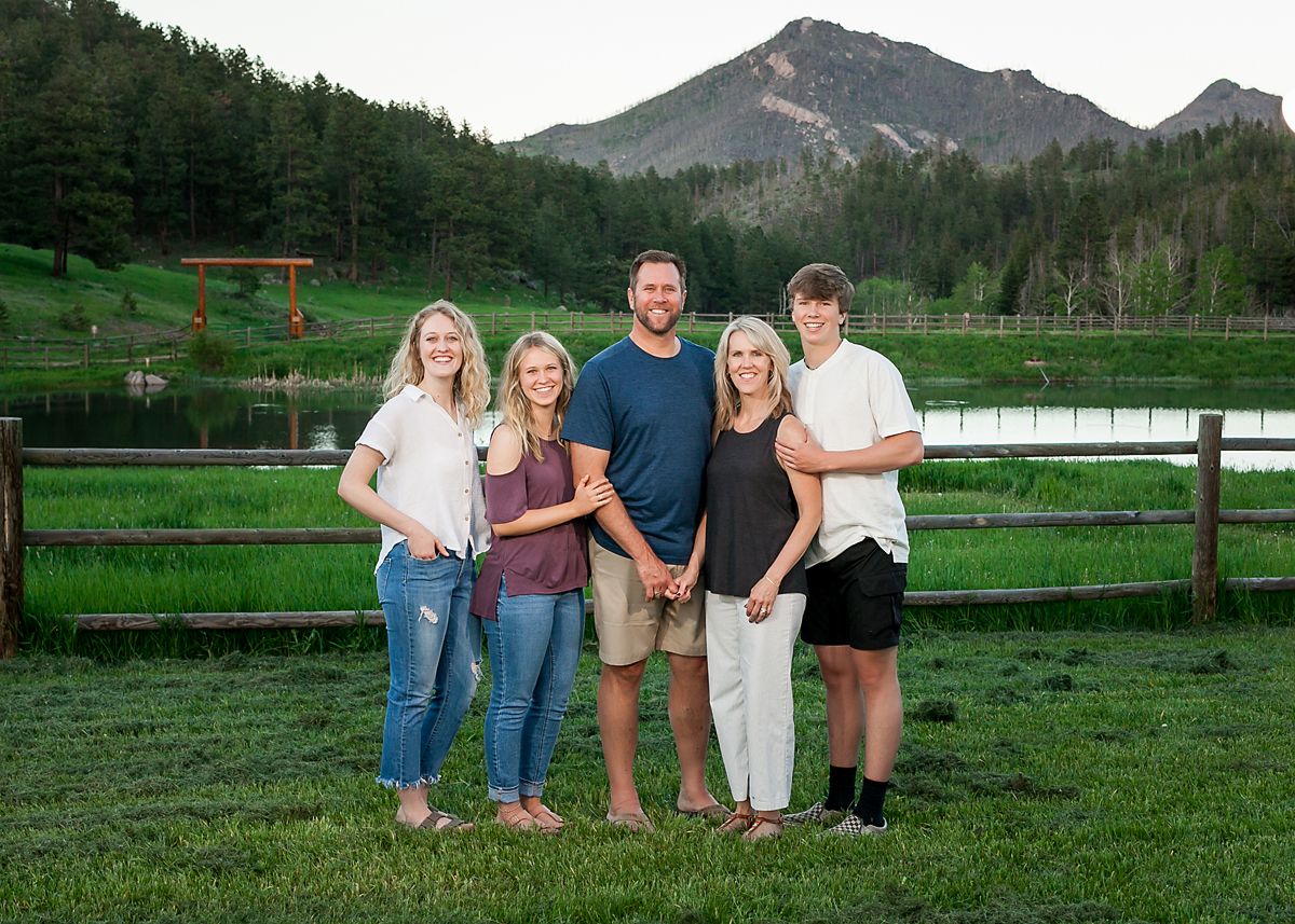Family of five standing together on a green lawn with a mountain lake backdrop.