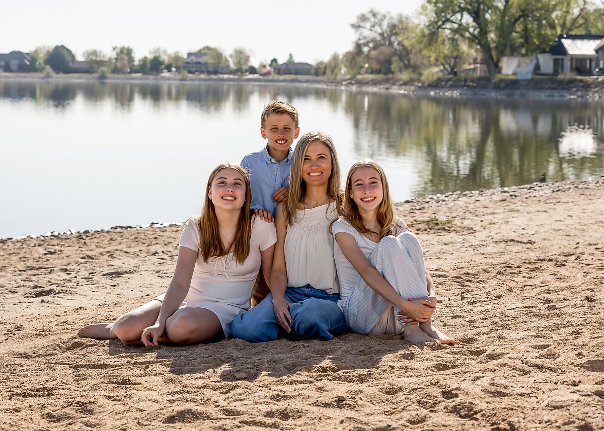 Happy family of four children sitting together on sandy beach with lake in background.