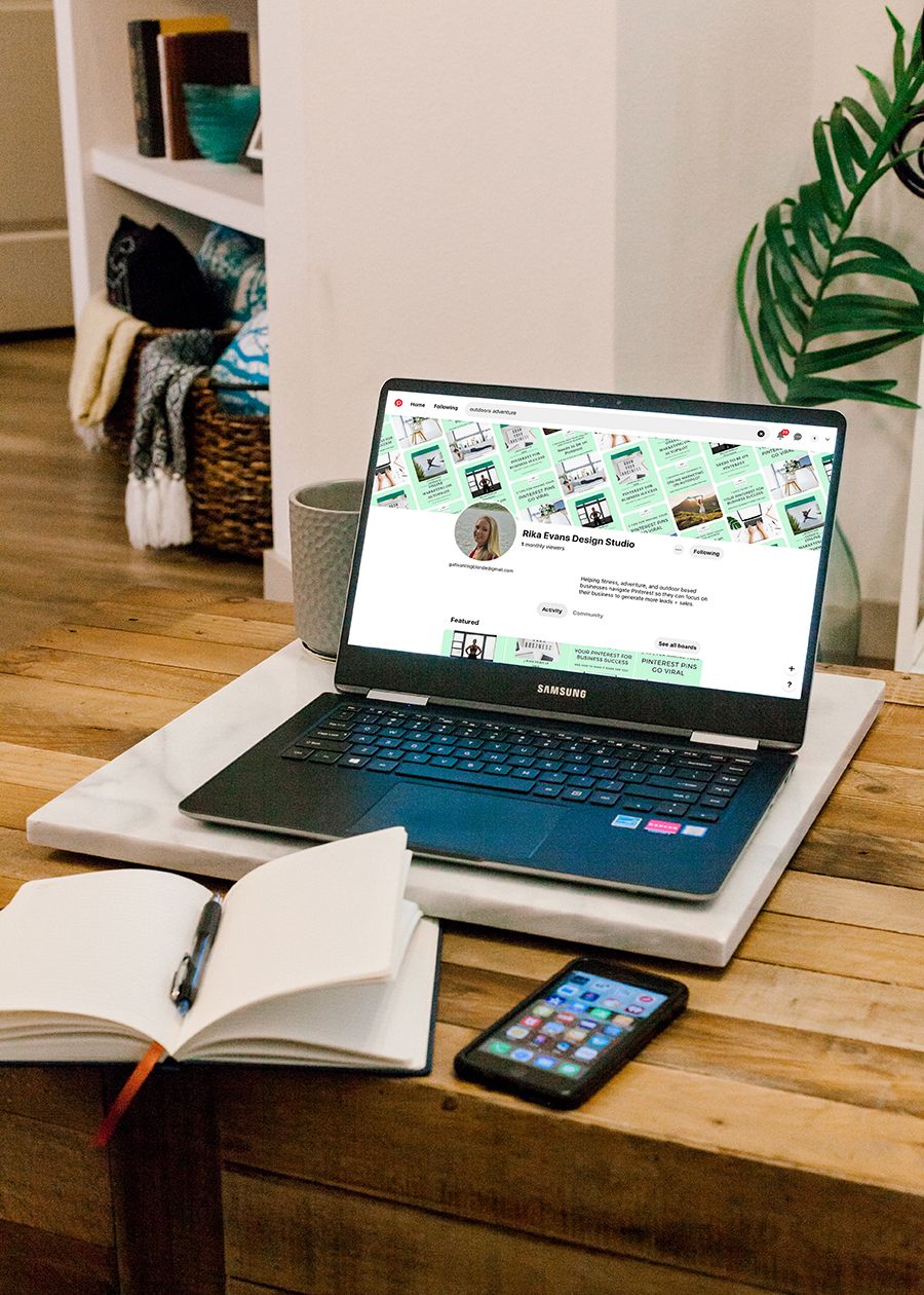 Samsung laptop on wooden desk displaying Pinterest profile, with open notebook, smartphone, and plant in cozy home office.