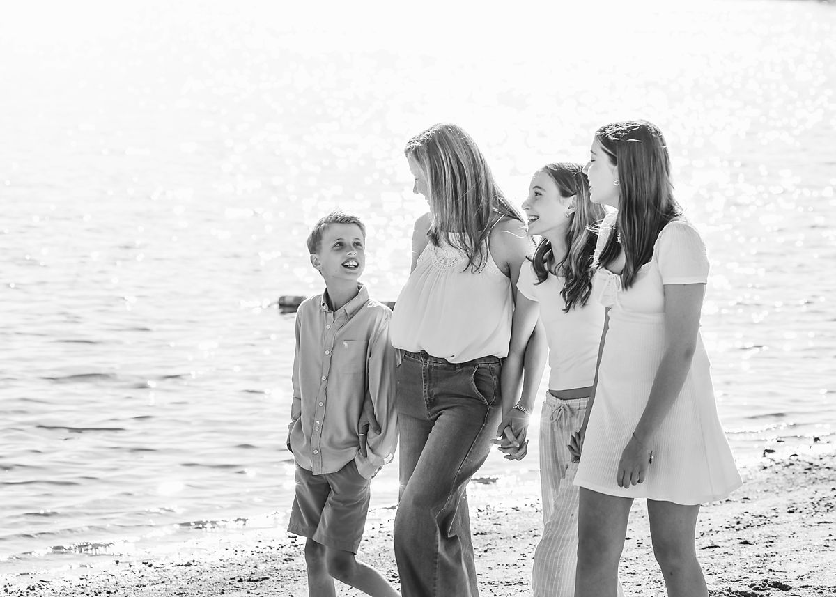 Black and white photo of a mother and three kids strolling along a lake shore.