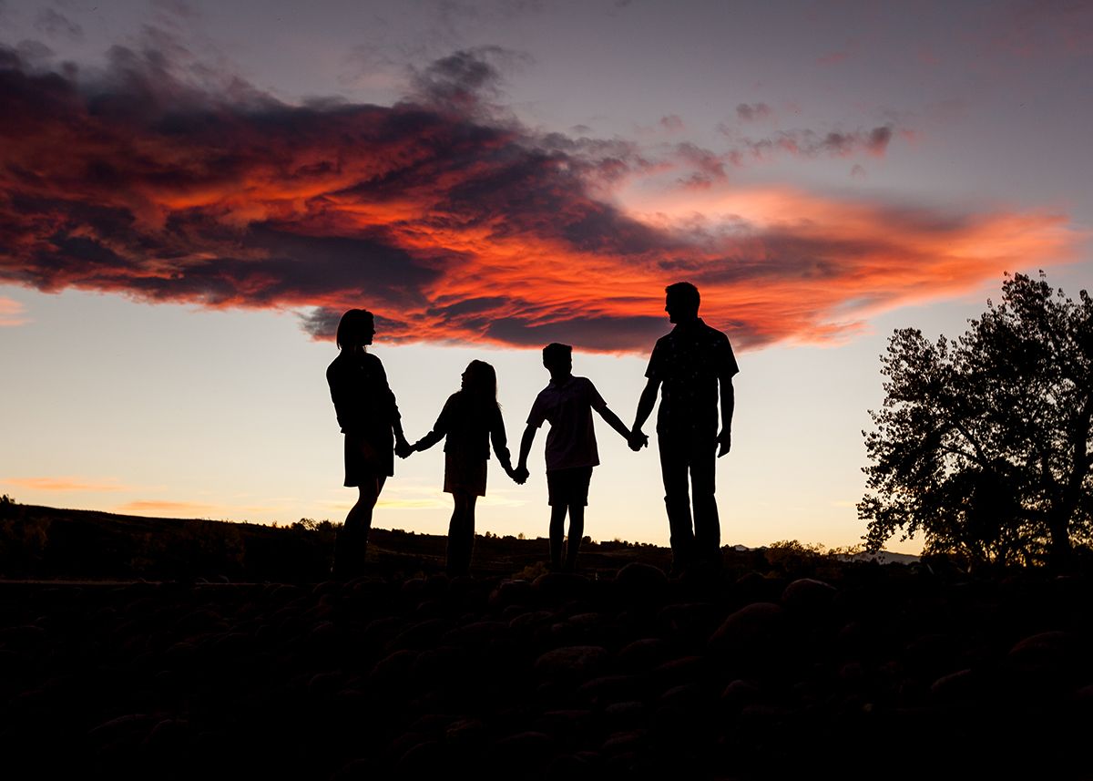 Silhouette of four family members holding hands against a dramatic red and orange sunset sky.