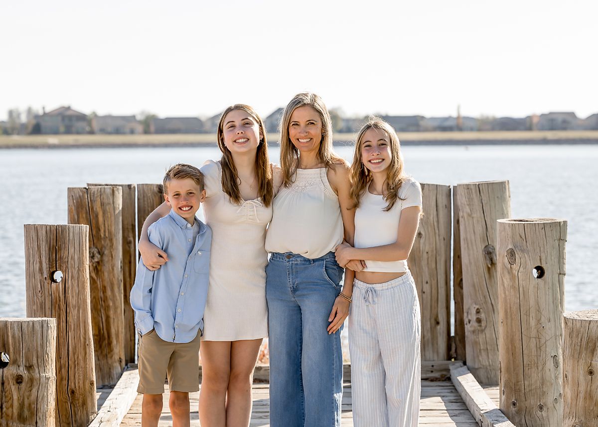 A mother smiles with her three children on a sunny waterfront dock.