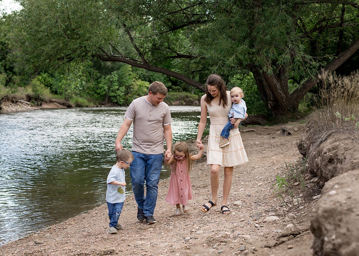 Family of five walking along a peaceful tree-lined riverbank together.