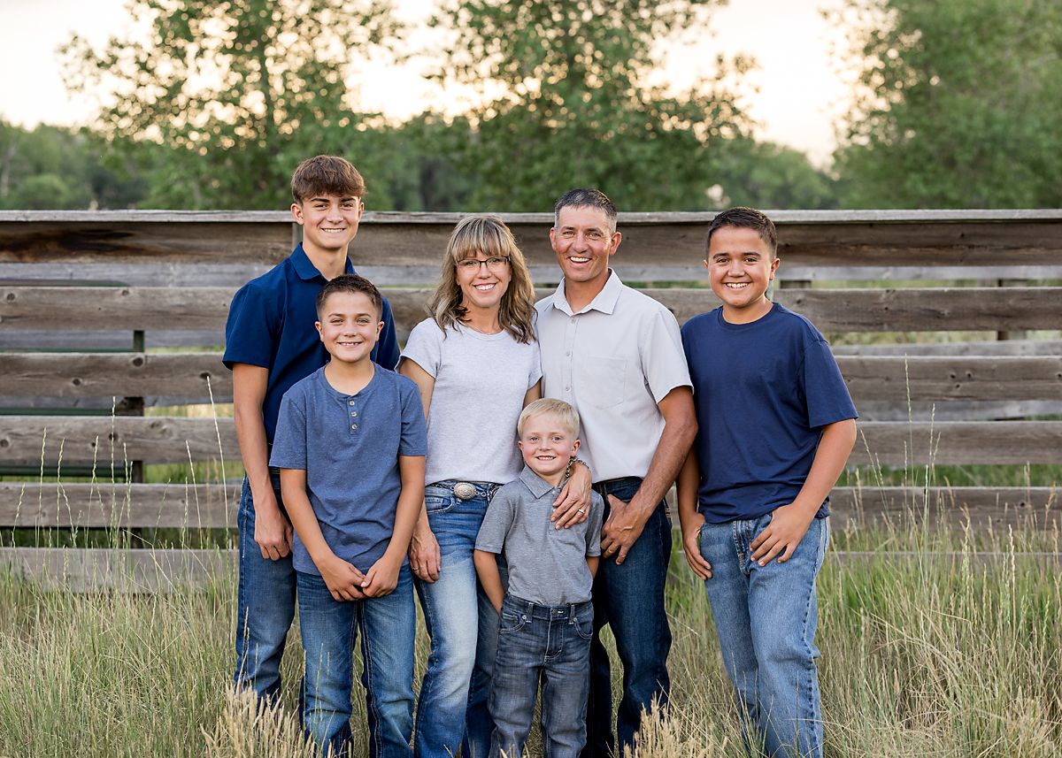 Family of six standing in tall grass near a rustic wooden fence.