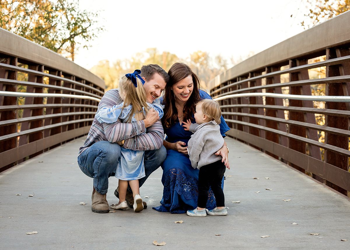 Happy family of four sharing a joyful moment on a wooden bridge surrounded by autumn trees.