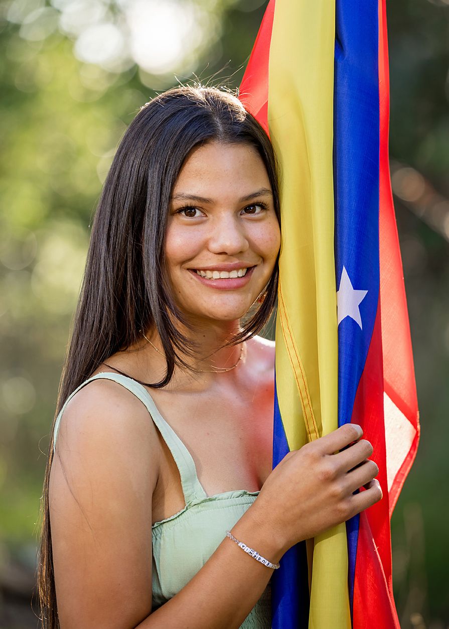 Smiling young woman holds colorful Venezuelan flag outdoors in natural light senior portrait photo.