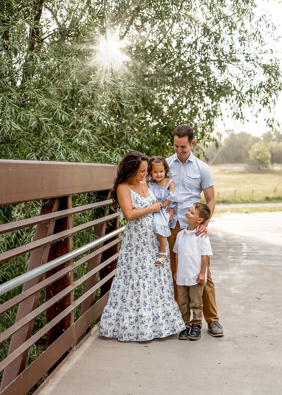 Family of four posing on a bridge surrounded by lush green trees during a golden hour outdoor photo session.
