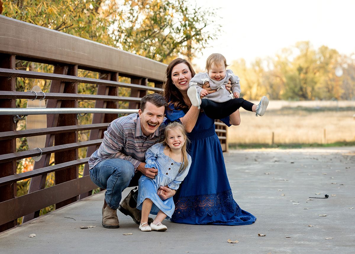 Happy family of four posing on a bridge during a fall outdoor photo session.