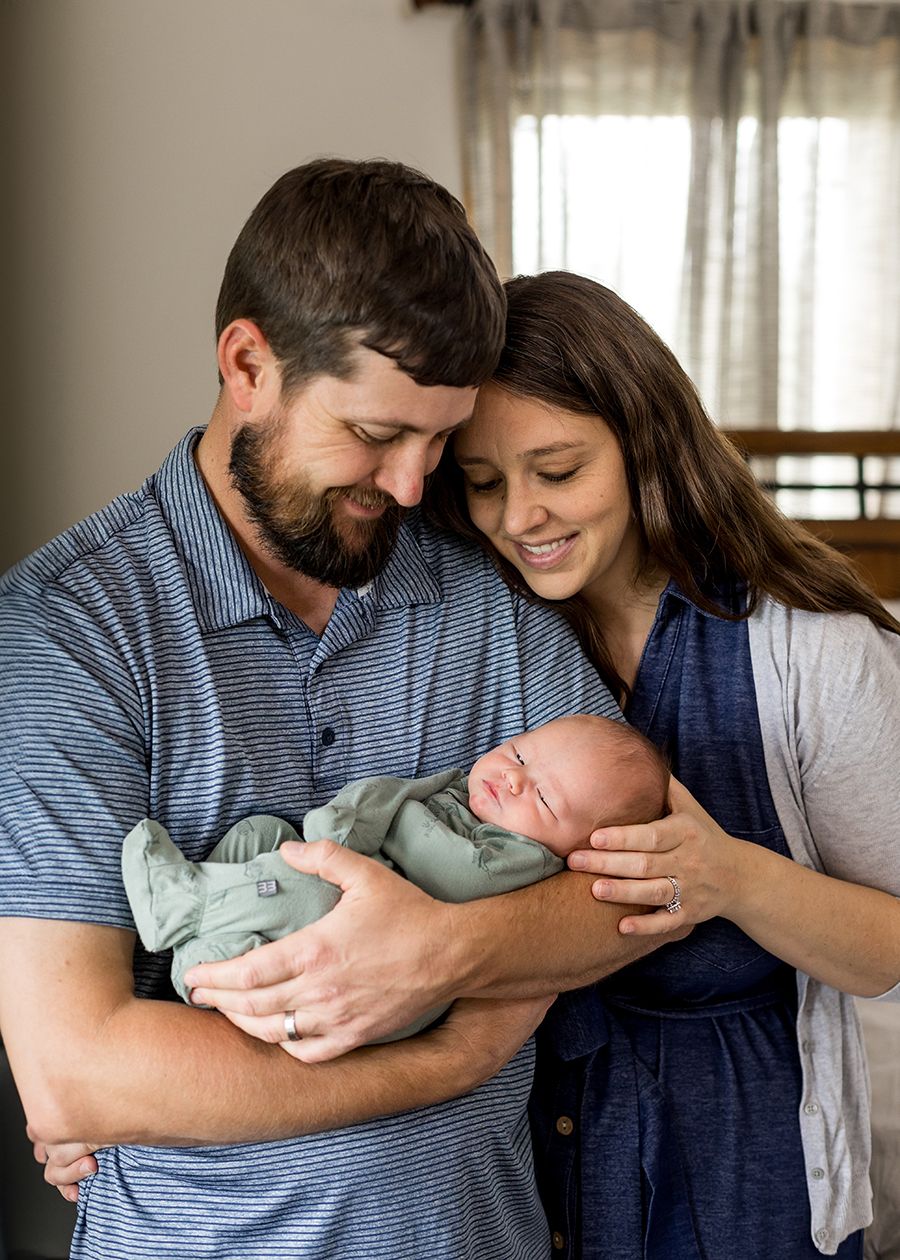 Happy parents holding their newborn baby wrapped in green swaddle blanket in a warm home setting.