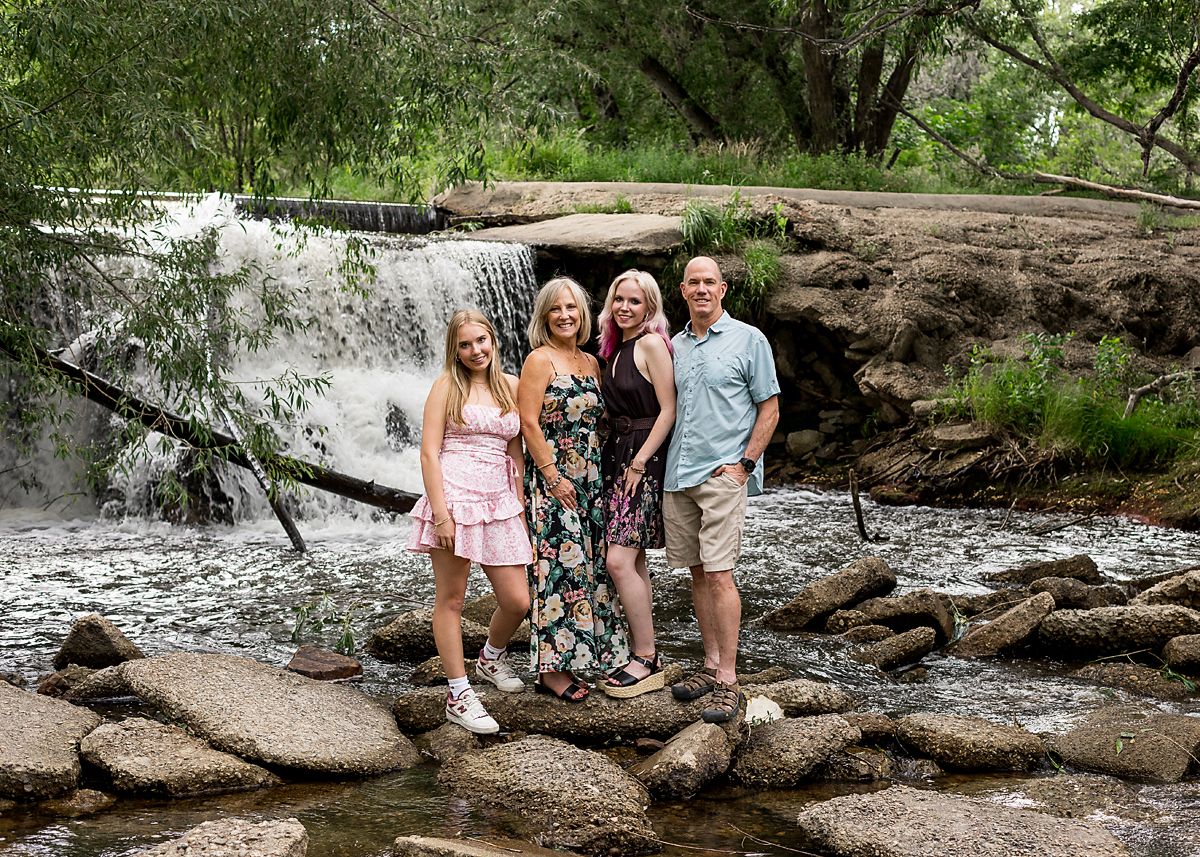 Family of four posing on rocks in front of a scenic waterfall.
