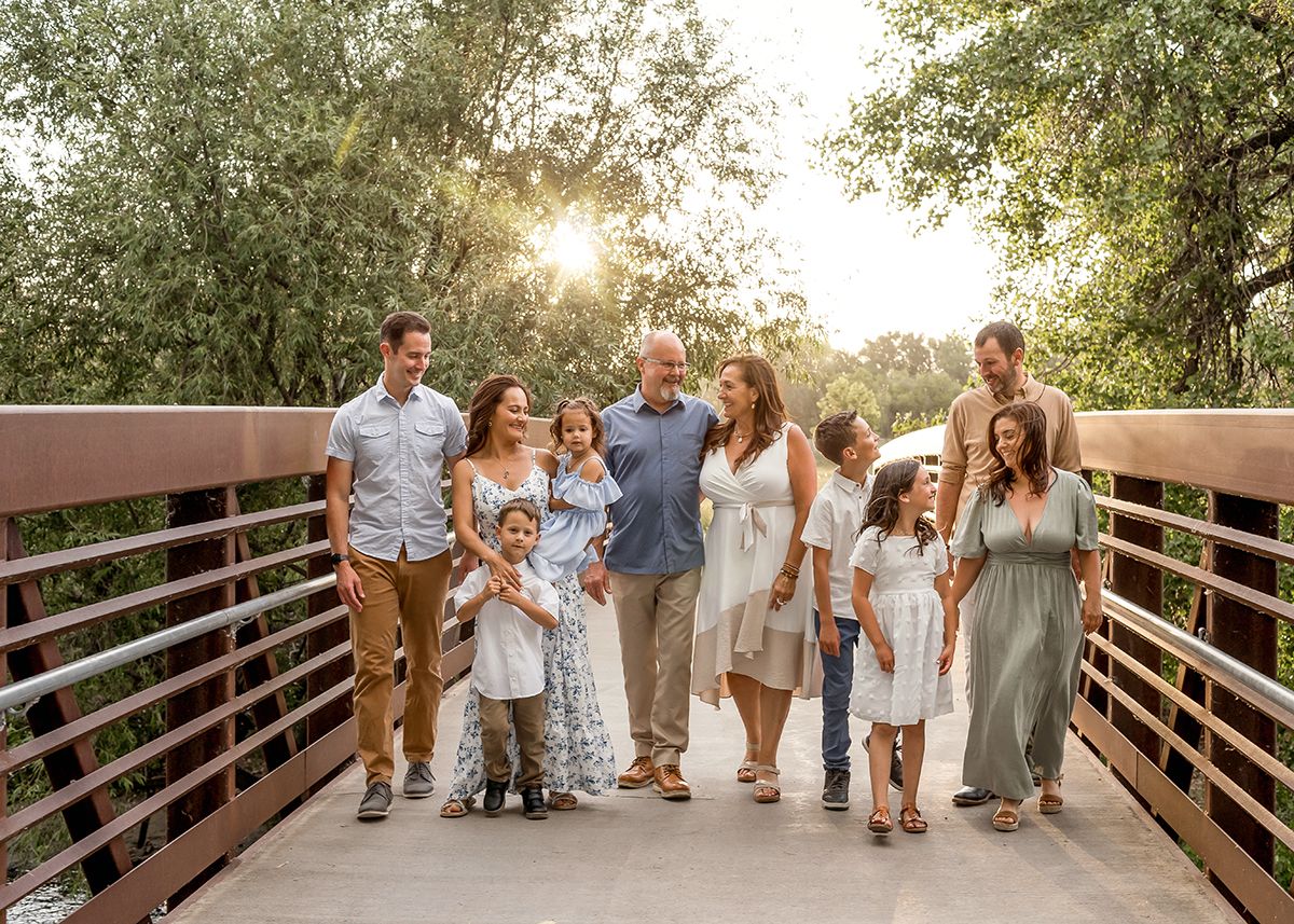 Large family walking together on a wooden bridge surrounded by lush green trees in warm golden sunlight.