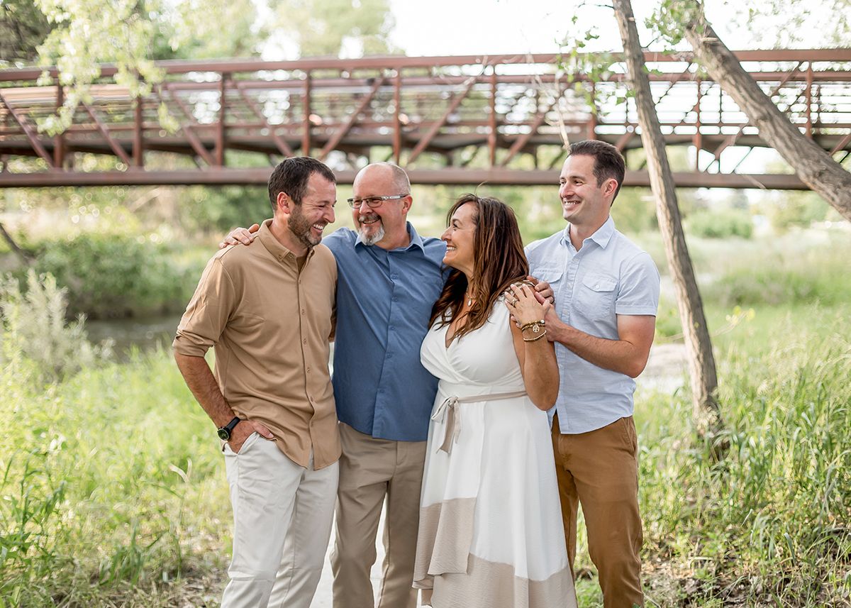 Happy family of four laughing together outdoors near a rustic bridge surrounded by lush greenery.