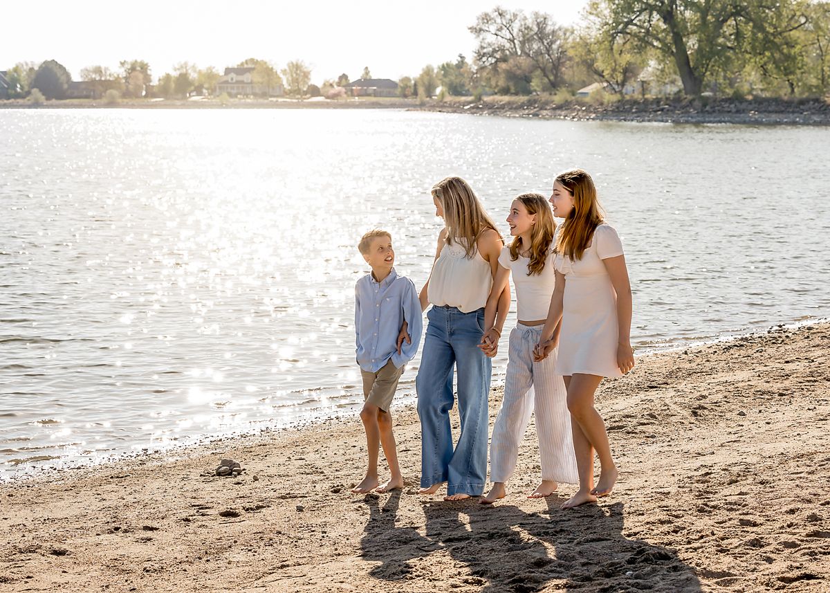 A mother and three children walk along a sandy lakeside beach together.
