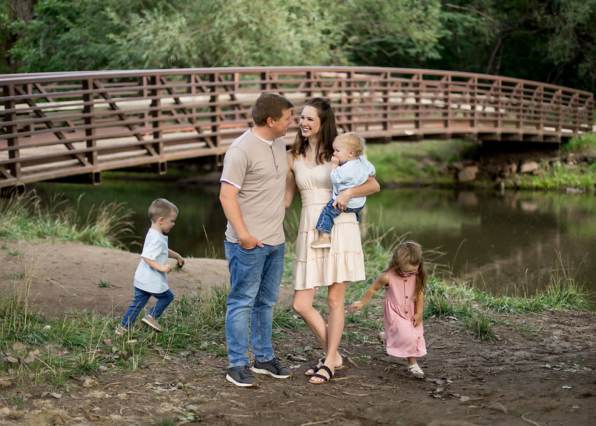 Young family of five sharing a tender moment near a wooden bridge over a peaceful creek outdoors.