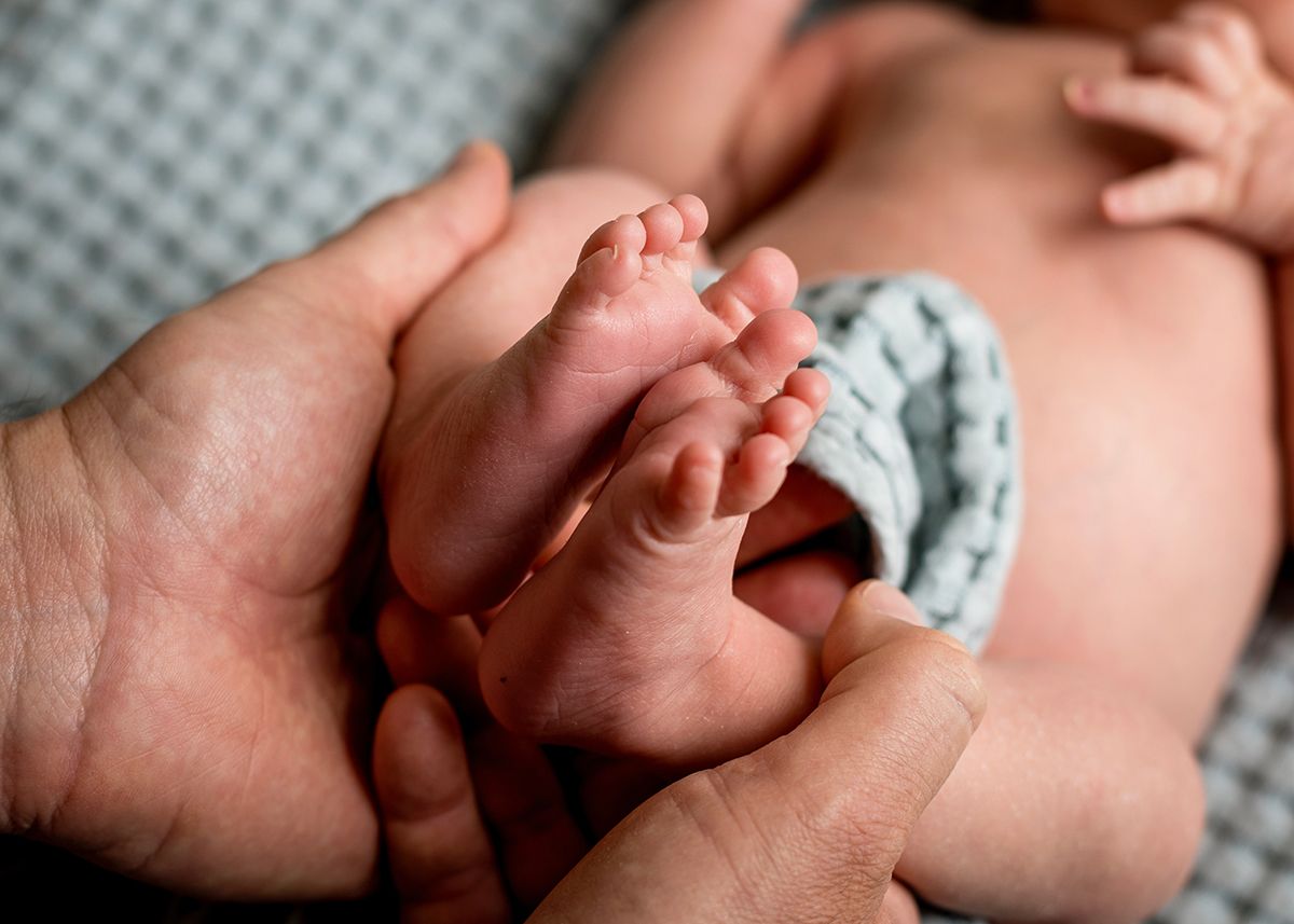 Adult hands gently holding tiny newborn baby feet, showcasing the delicate size difference between parent and infant.