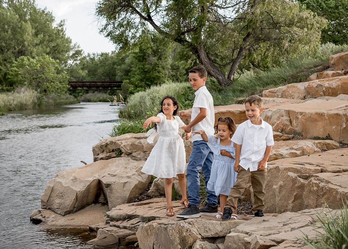 Family of four posing on rocky riverbank surrounded by lush green trees, wearing coordinated white outfits.