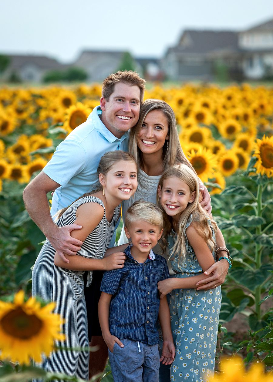 Family of five smiling in a sunflower field during golden hour.