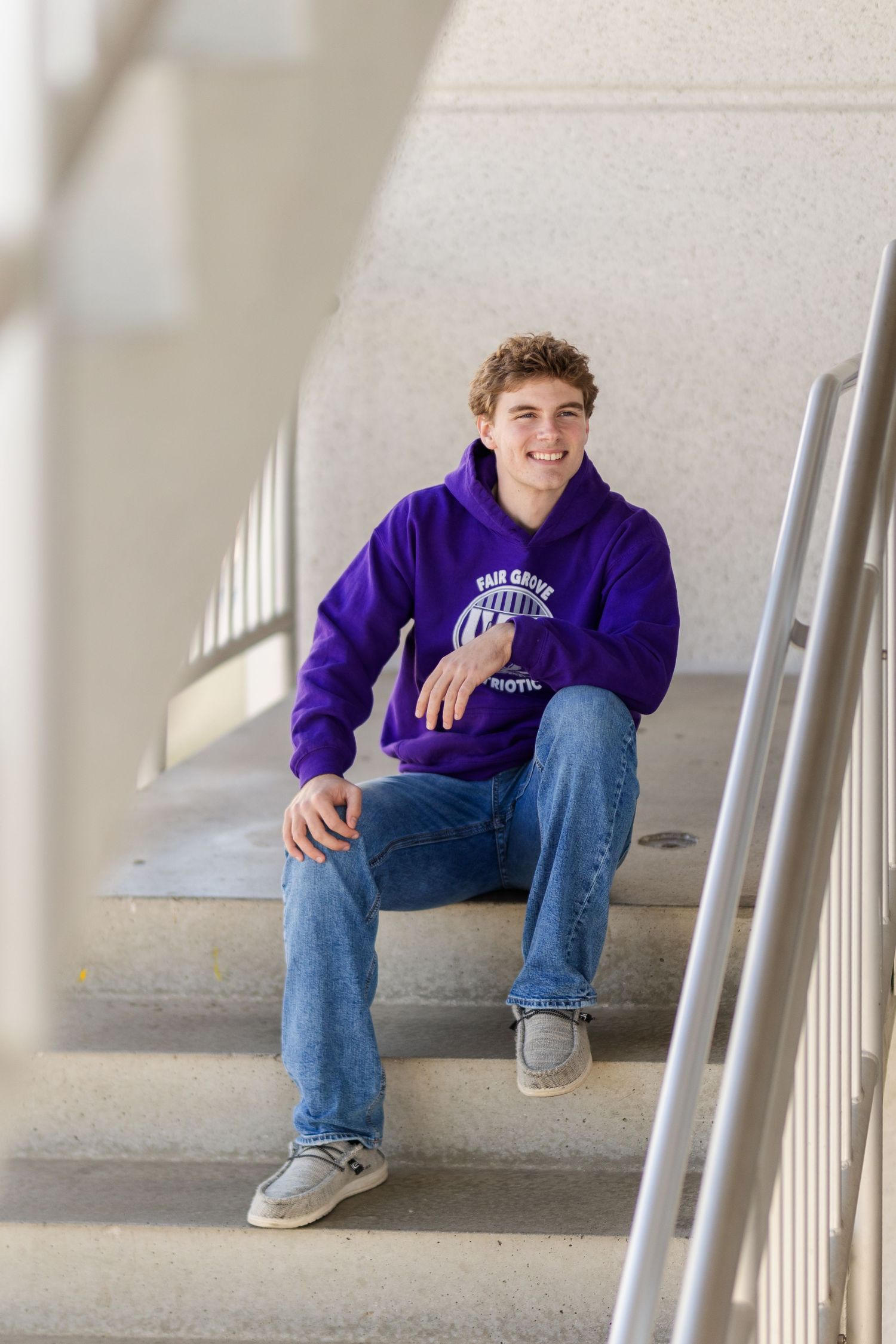 A casual portrait on white concrete stairs featuring someone in a purple school spirit hoodie and jeans.
