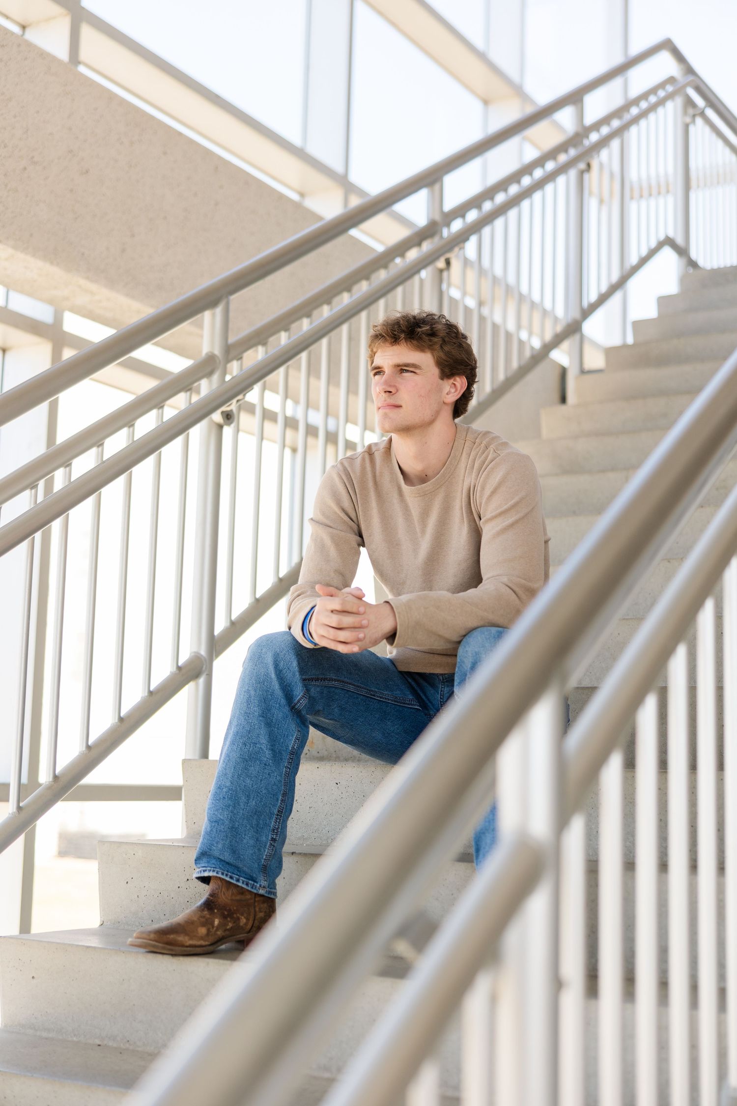 A student sits on concrete stairs in a beige sweater and jeans while looking contemplatively to the side.