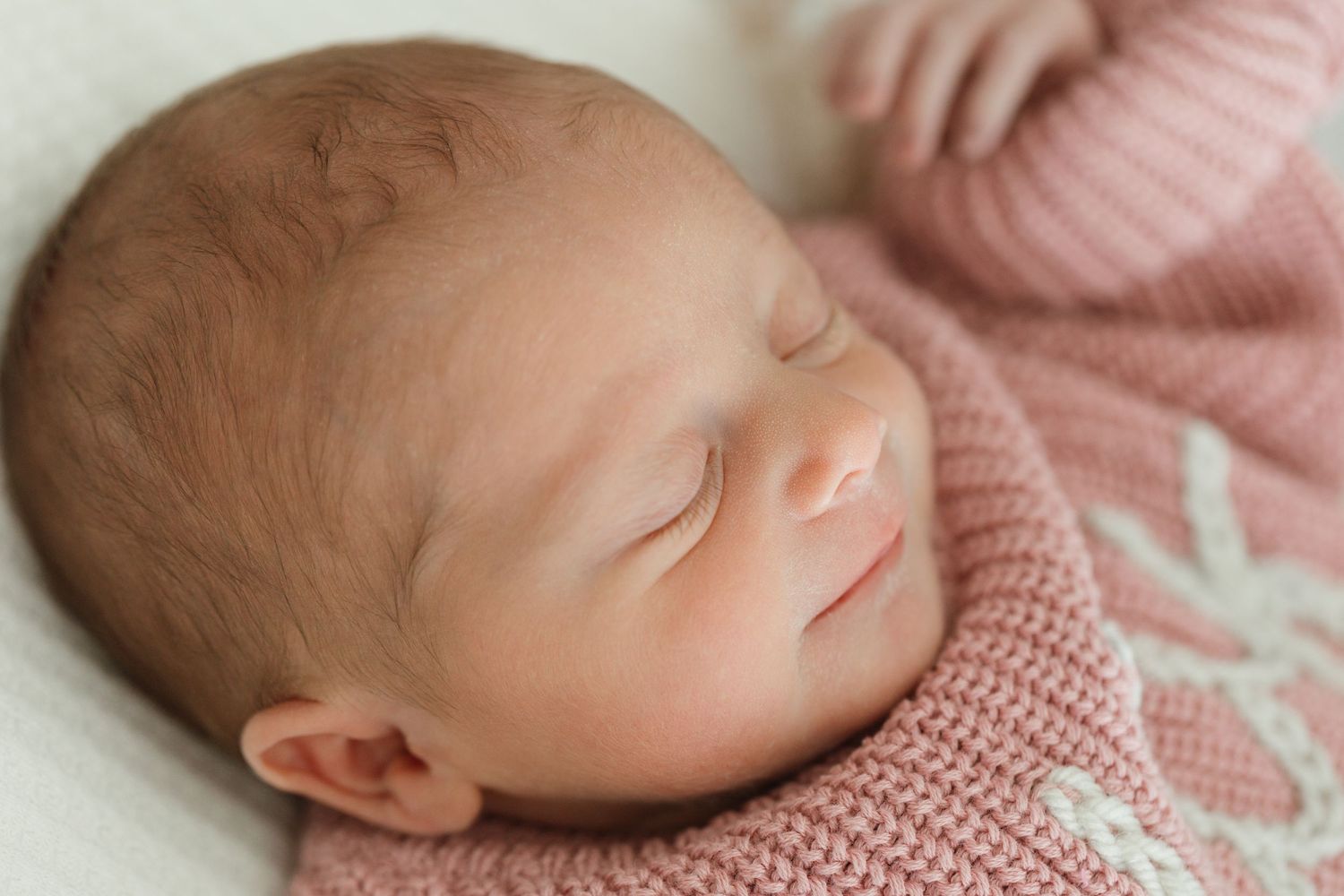 A peaceful sleeping newborn baby wearing a soft pink knitted sweater.