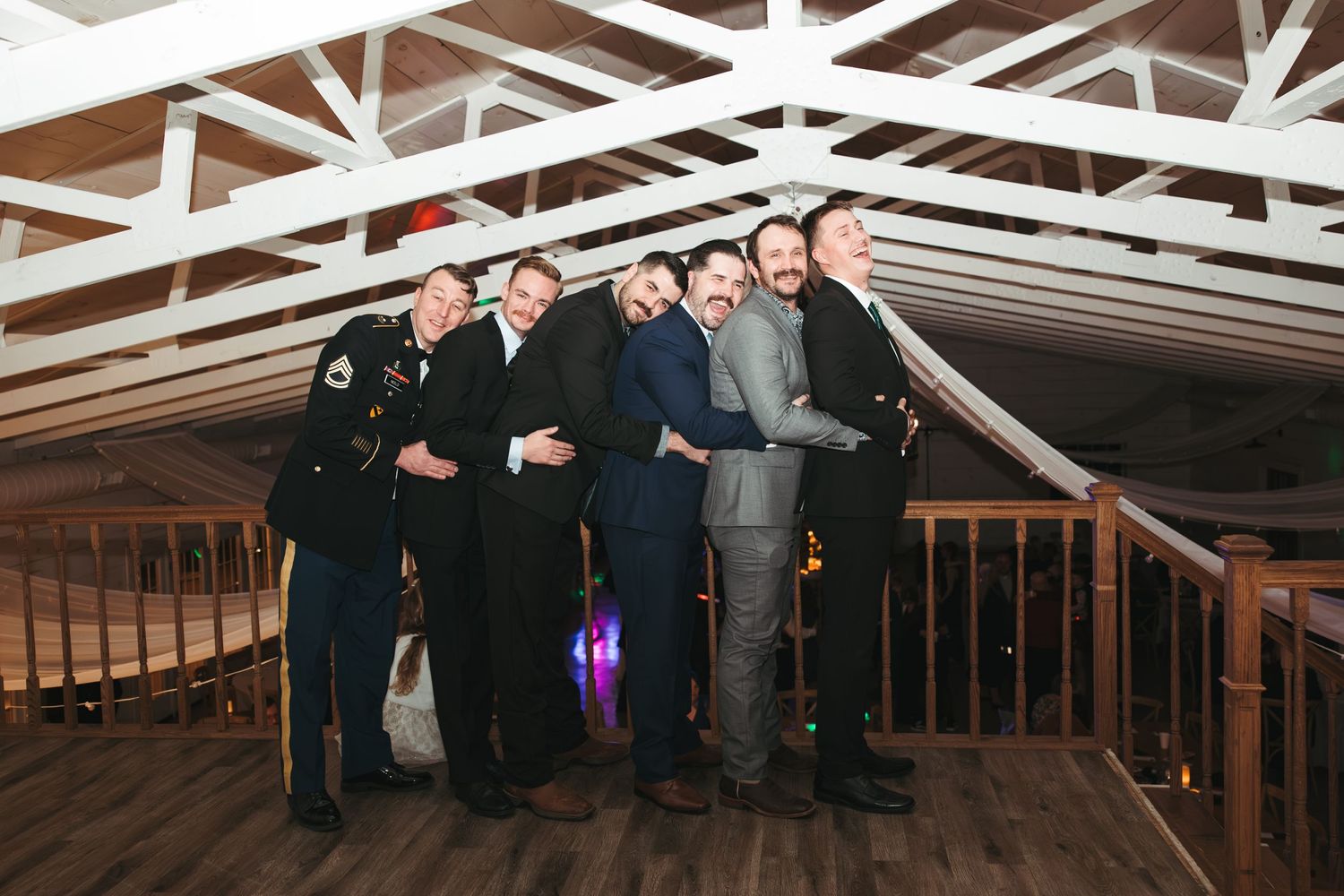 Group of formally dressed people pose together under white wooden beams.