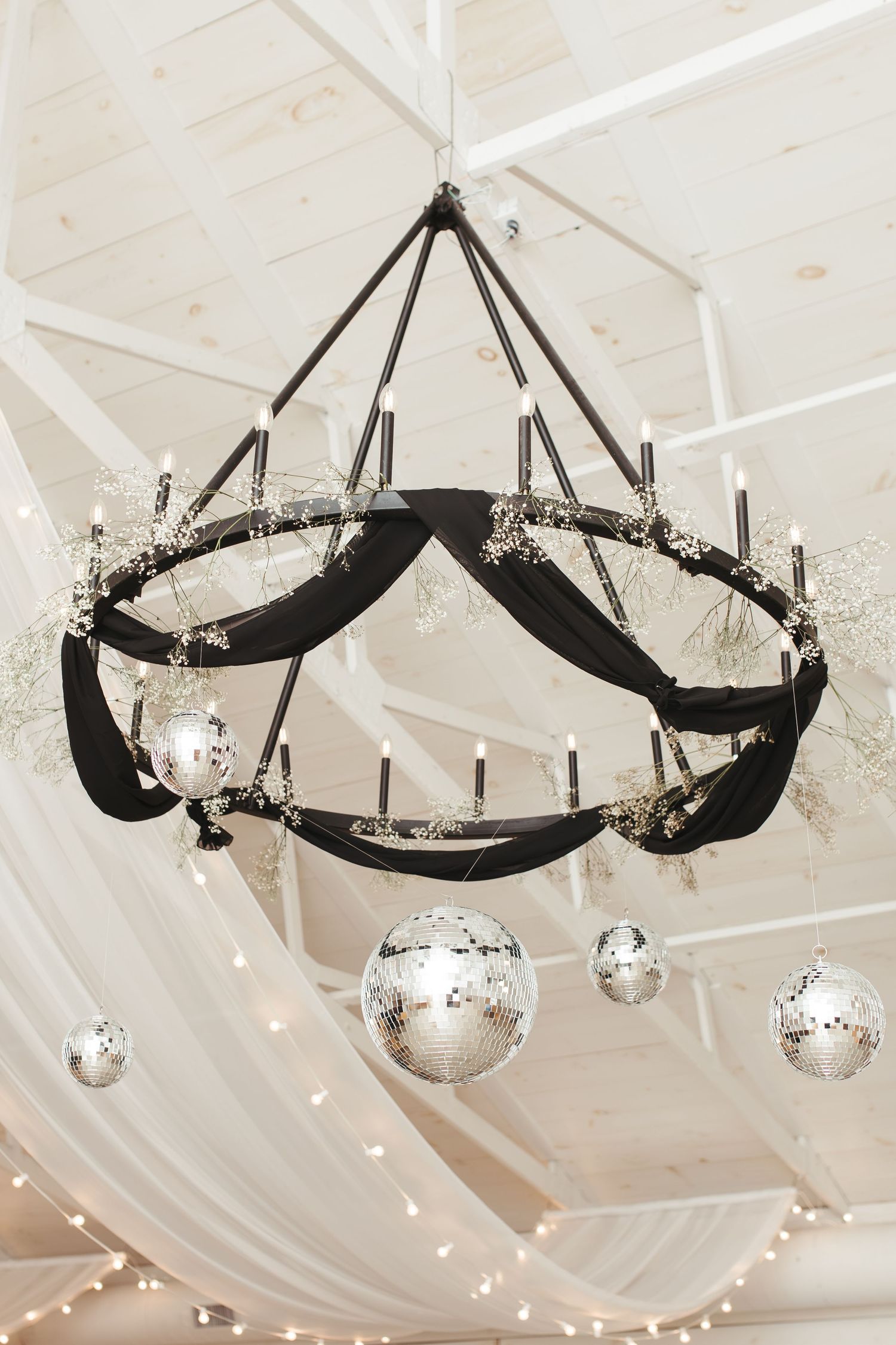 An elegant black chandelier with disco balls and crystal decorations hanging from a white ceiling.