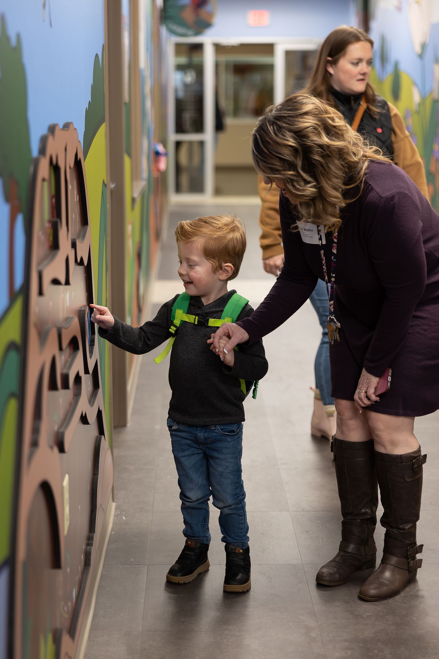 A child explores a colorful hallway wall mural while accompanied by an adult.