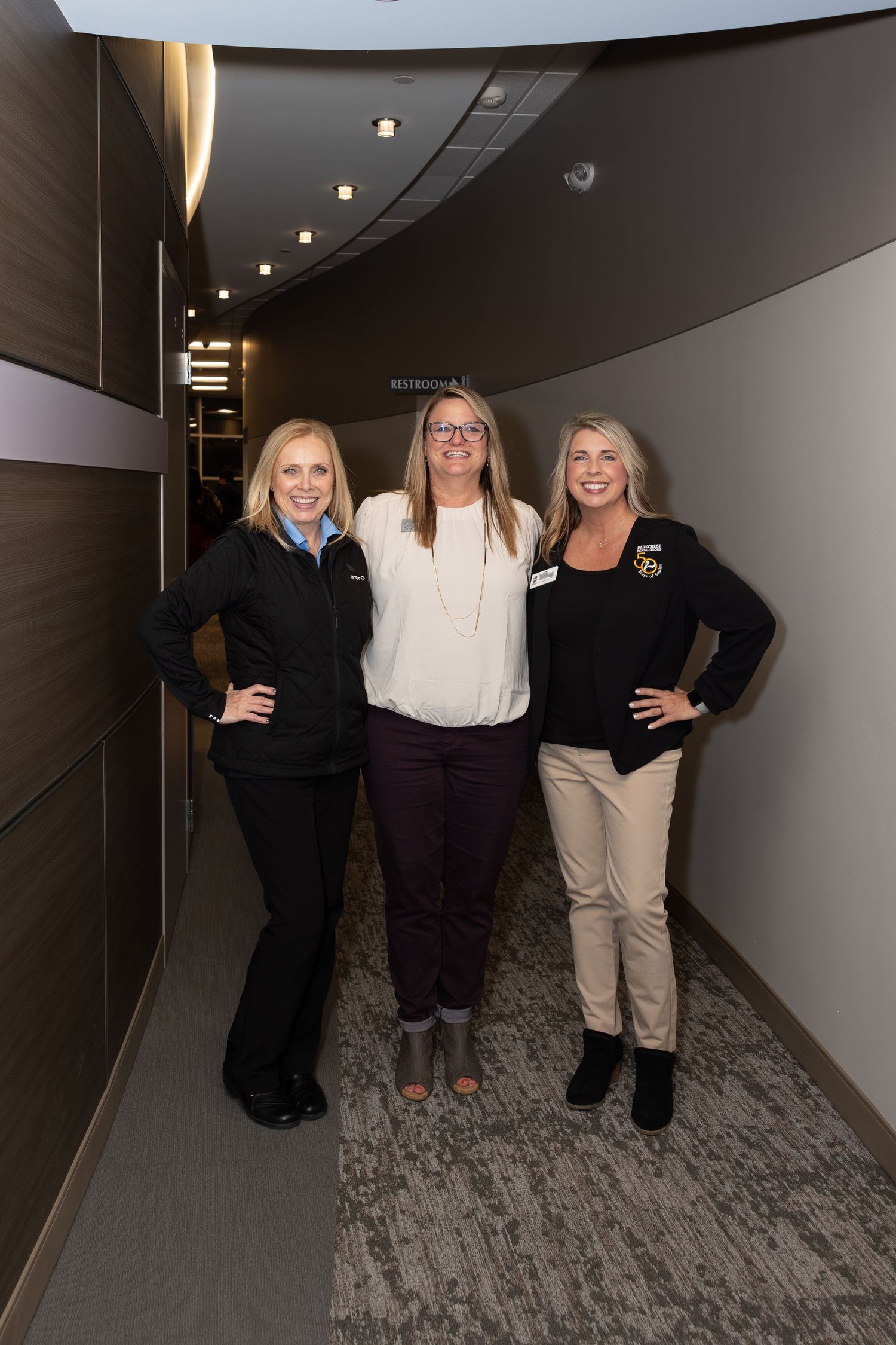 Three colleagues pose together in modern office hallway.