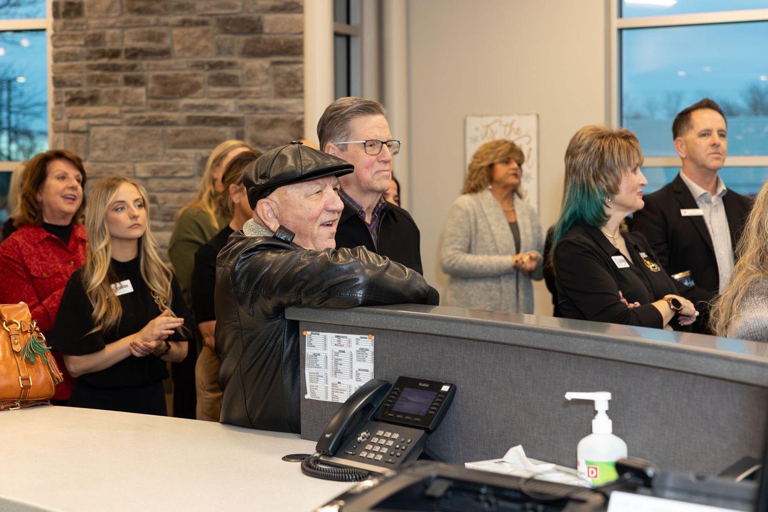 Office celebration with staff members gathered at reception desk with stone walls and hand sanitizer.