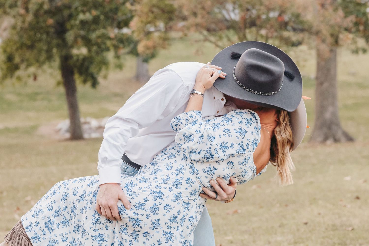Romantic dip pose between couple in western attire under autumn trees.