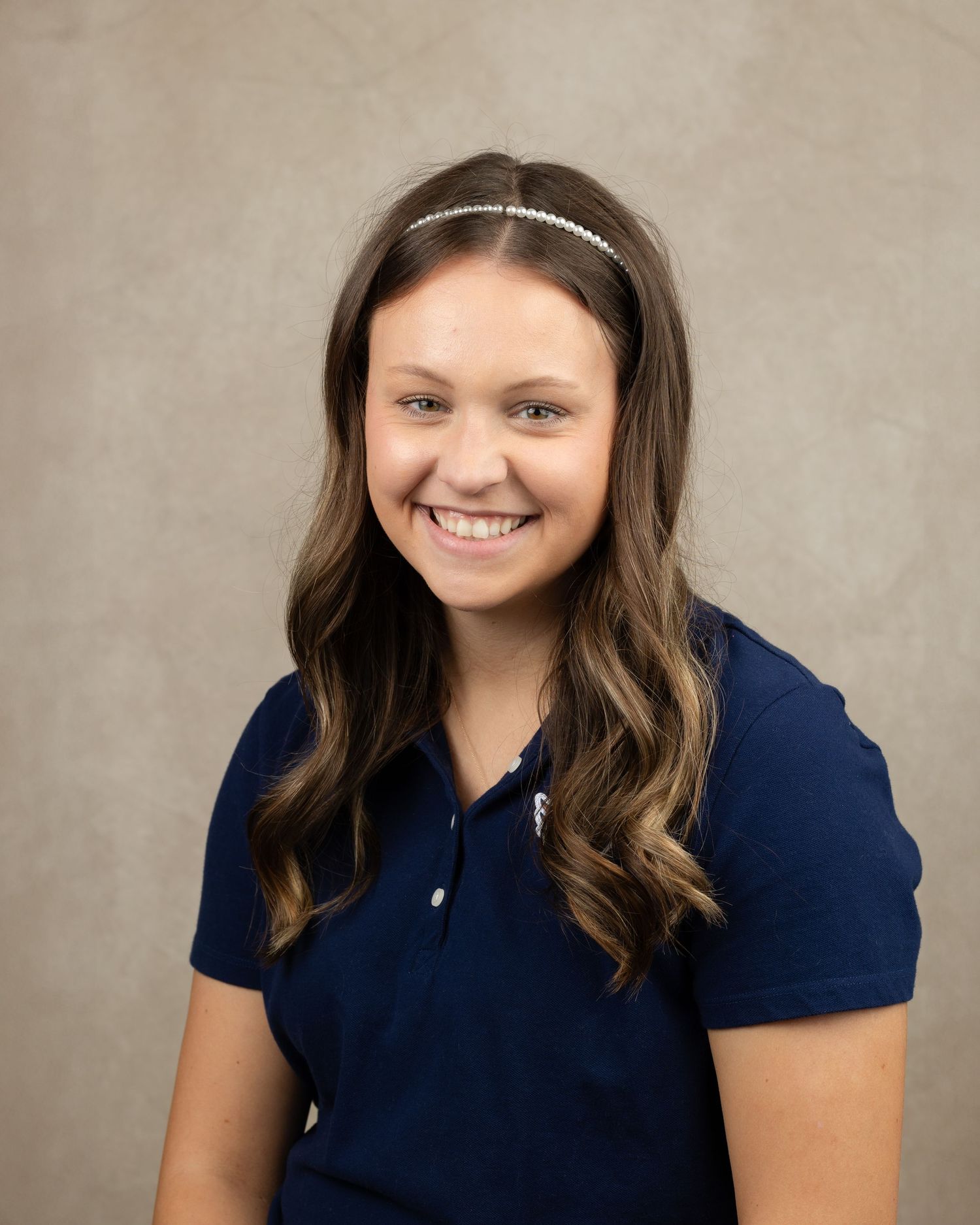 Professional headshot of woman in navy polo with sparkly headband and wavy hair.