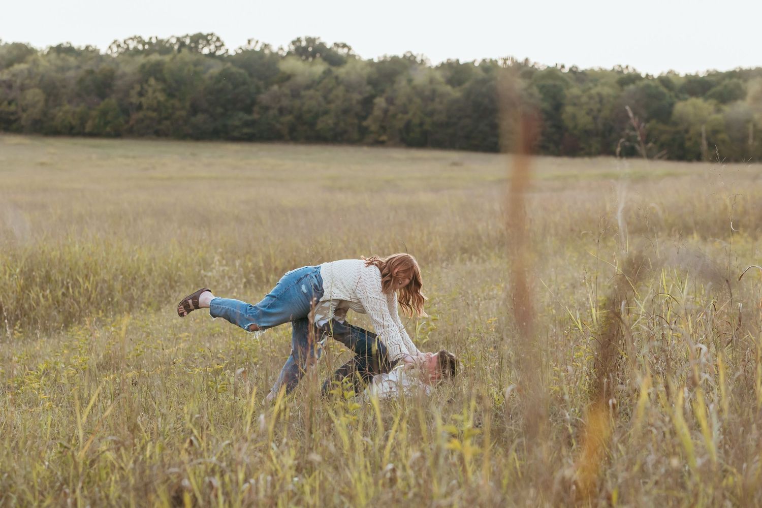 Person leaning forward in a meadow during golden hour with trees in background.