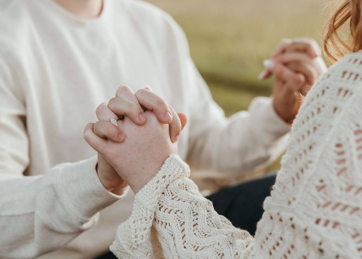 Close-up of hands clasped together wearing white knit sweaters.