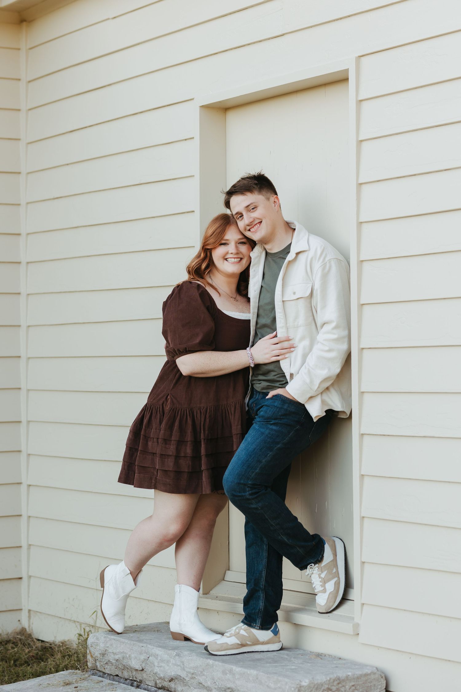 Happy couple laughing together while standing on concrete step by white building.
