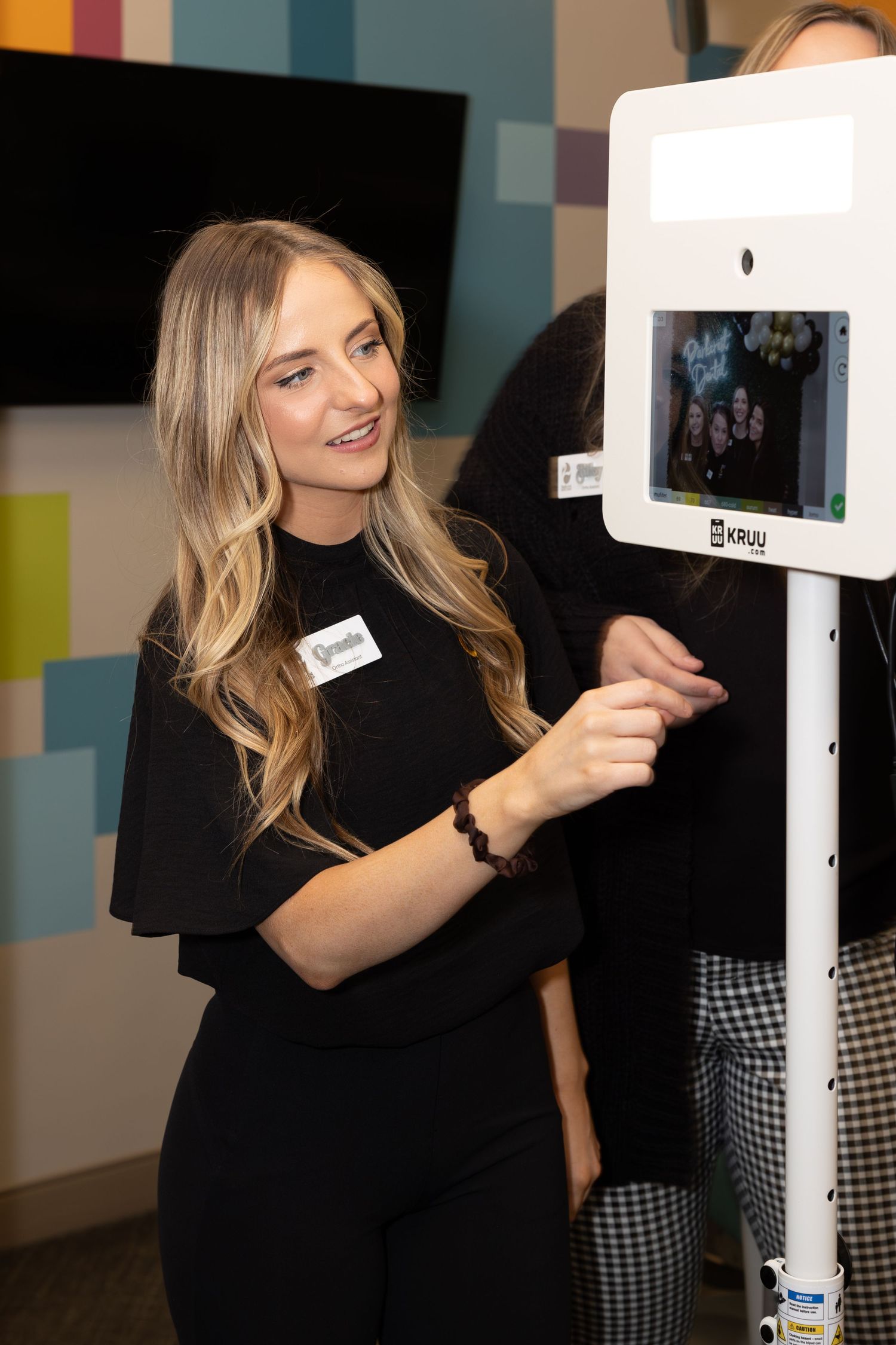 A person in black clothing interacts with a digital display against a colorful wall.