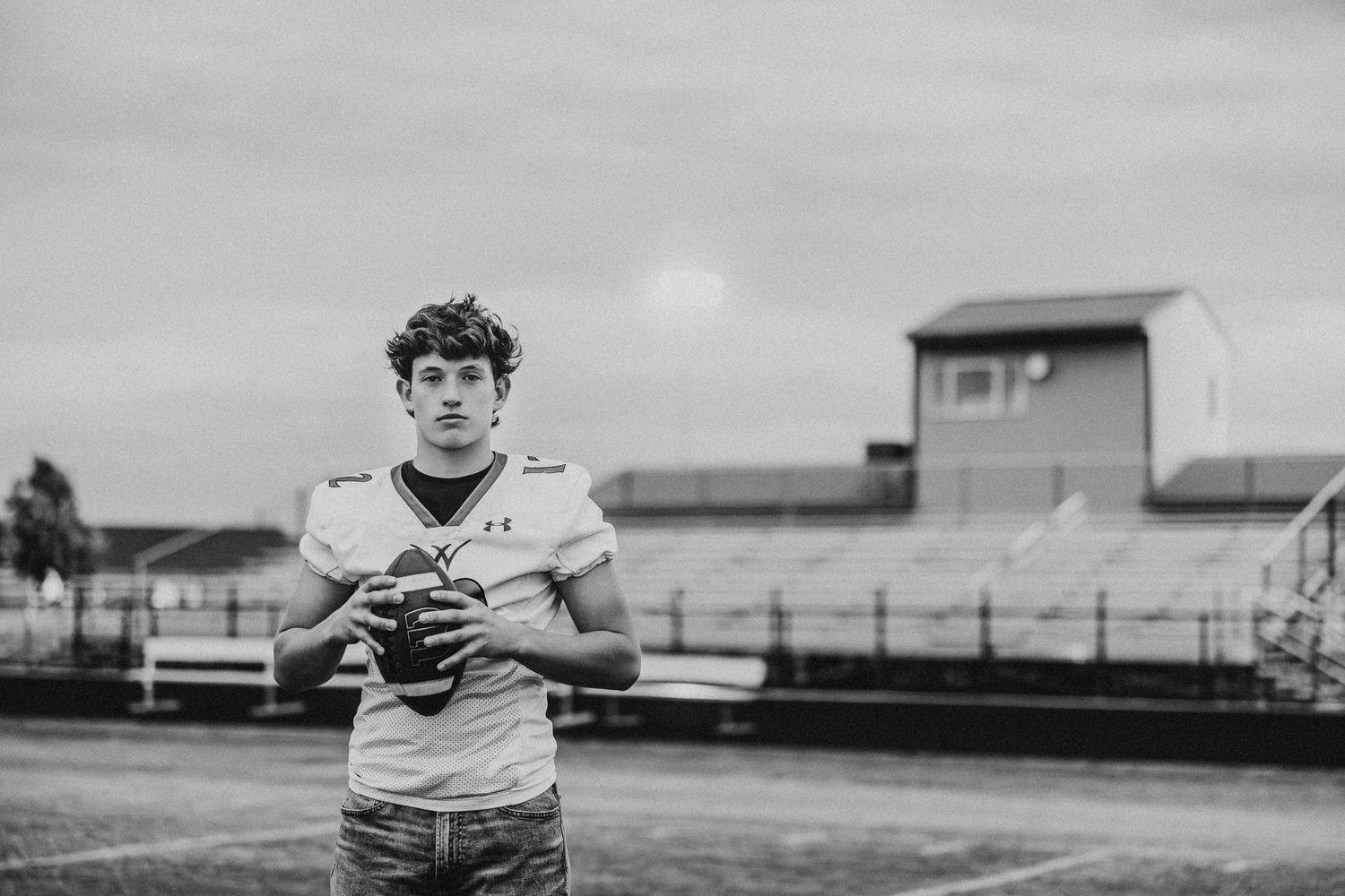 Quarterback practices throwing drills on empty football field in monochrome.