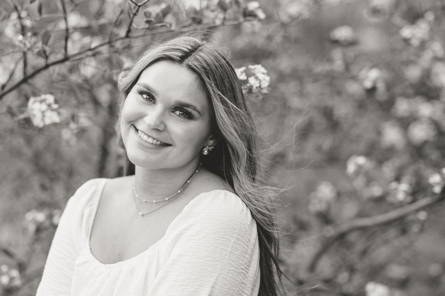 Black and white portrait with light layered hair against blooming flowers.