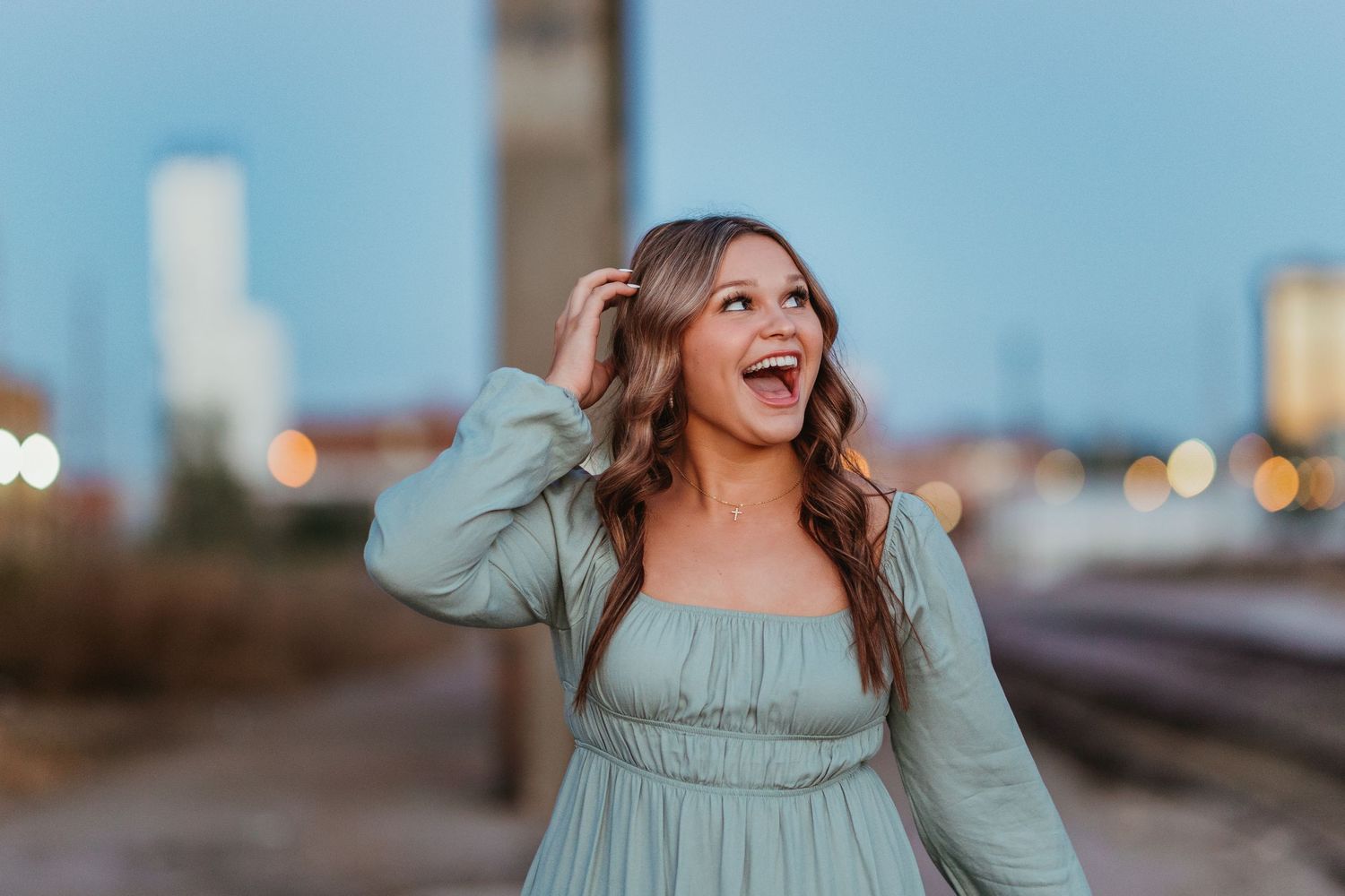 Person in mint dress laughs joyfully against urban cityscape background.