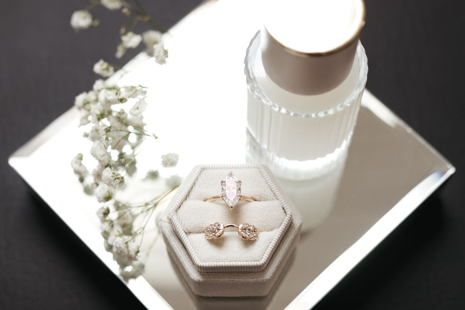 Wedding rings displayed in a hexagonal box with baby's breath flowers and white decor.