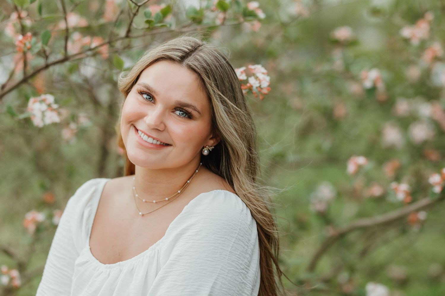 Portrait of woman in white top against blossoming spring foliage background.