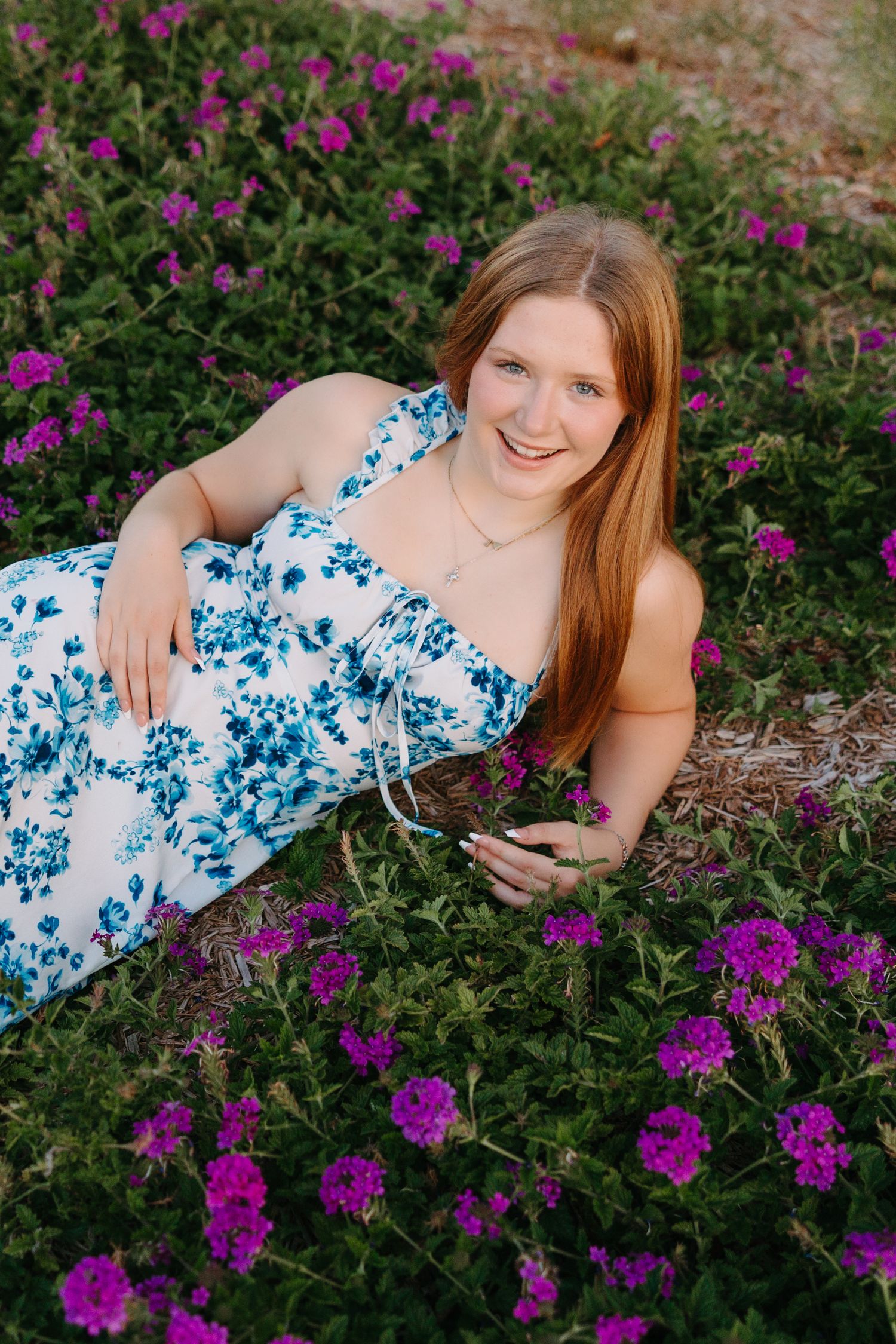 Someone wearing a blue and white floral dress lying among purple wildflowers in a natural garden setting.